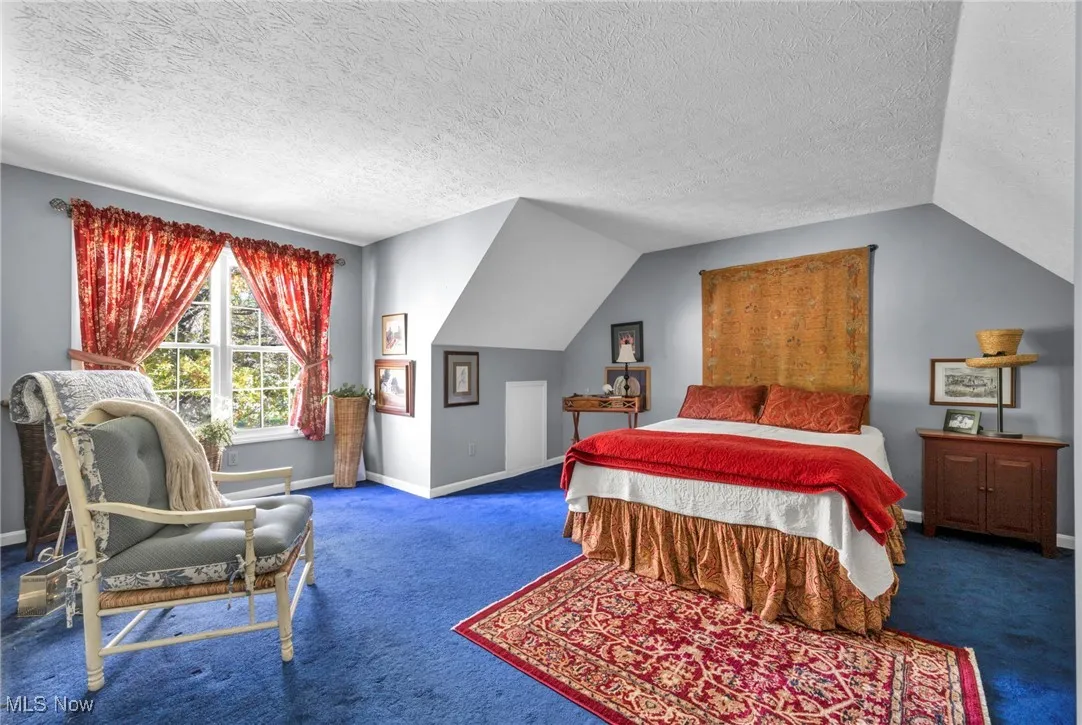 Bedroom with vaulted ceiling, a textured ceiling, and carpet flooring