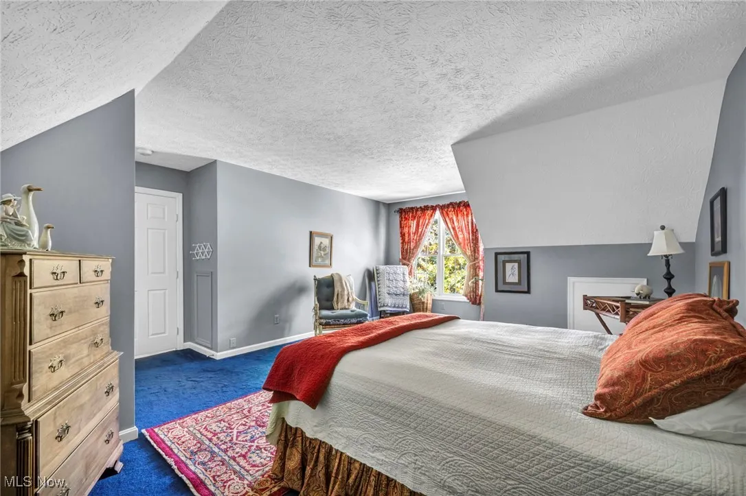 Bedroom with a textured ceiling, dark colored carpet, and vaulted ceiling