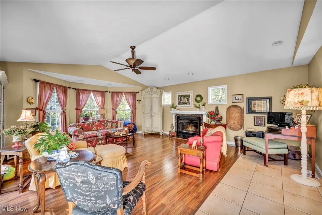Living room with lofted ceiling, a fireplace with flush hearth, light wood finished floors, and ceiling fan