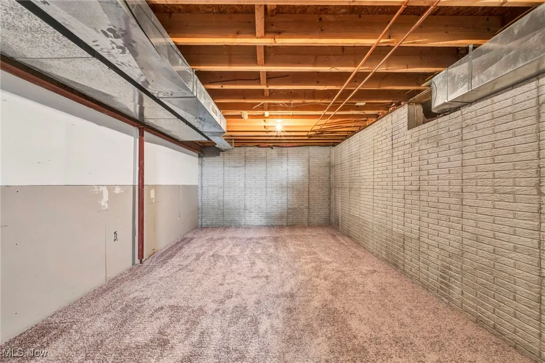Unfinished below grade area with carpet floors and brick wall