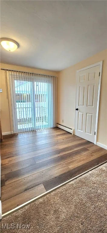 Unfurnished room with a baseboard heating unit and wood finished floors