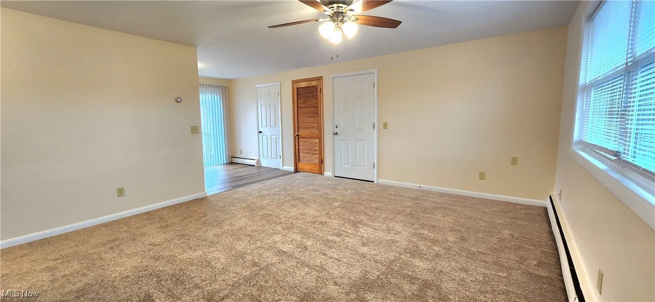 Carpeted empty room with baseboard heating, healthy amount of natural light, a ceiling fan, and a baseboard radiator