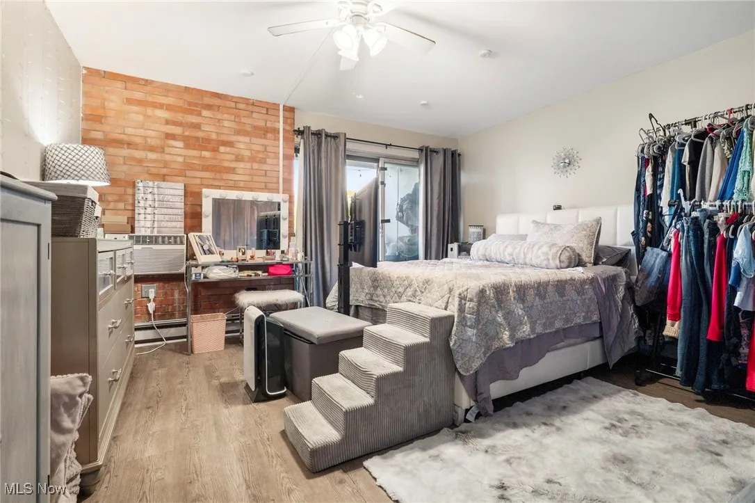 Bedroom featuring light wood-style flooring, ceiling fan, a baseboard heating unit, brick wall, and access to outside