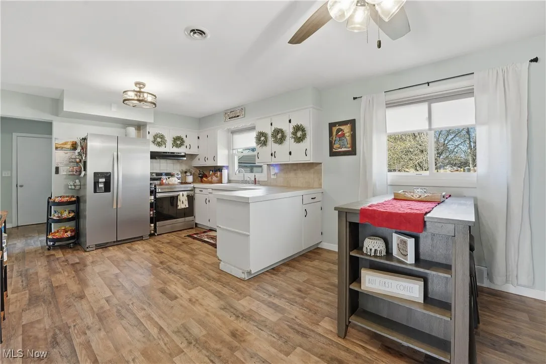 Kitchen featuring light countertops, white cabinetry, appliances with stainless steel finishes, backsplash, and light wood-style floors