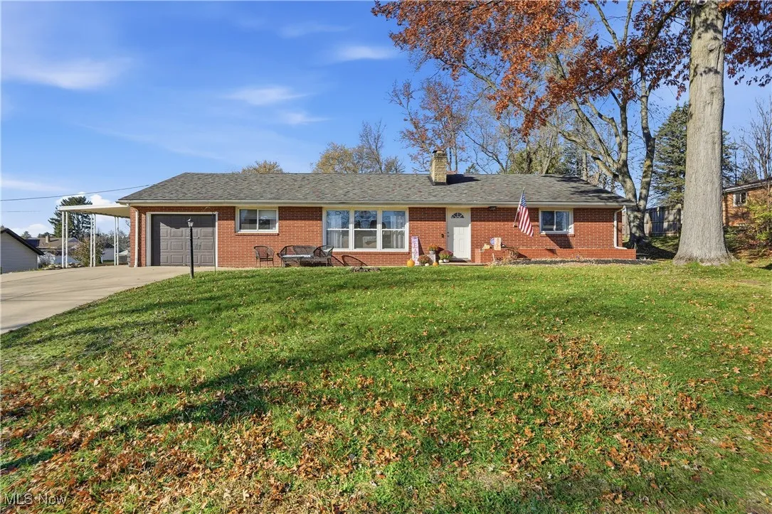Ranch-style home featuring driveway, brick siding, a chimney, a front yard, and a garage