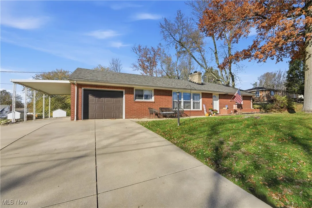 Ranch-style house with a front yard, brick siding, a chimney, driveway, and an attached carport