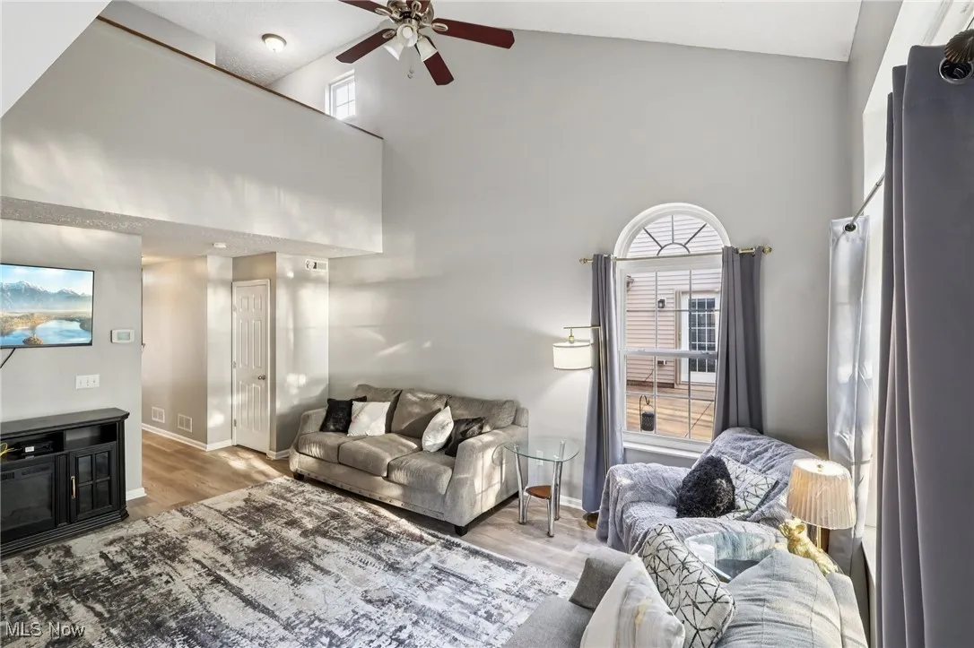 Living area with high vaulted ceiling, a ceiling fan, and wood finished floors
