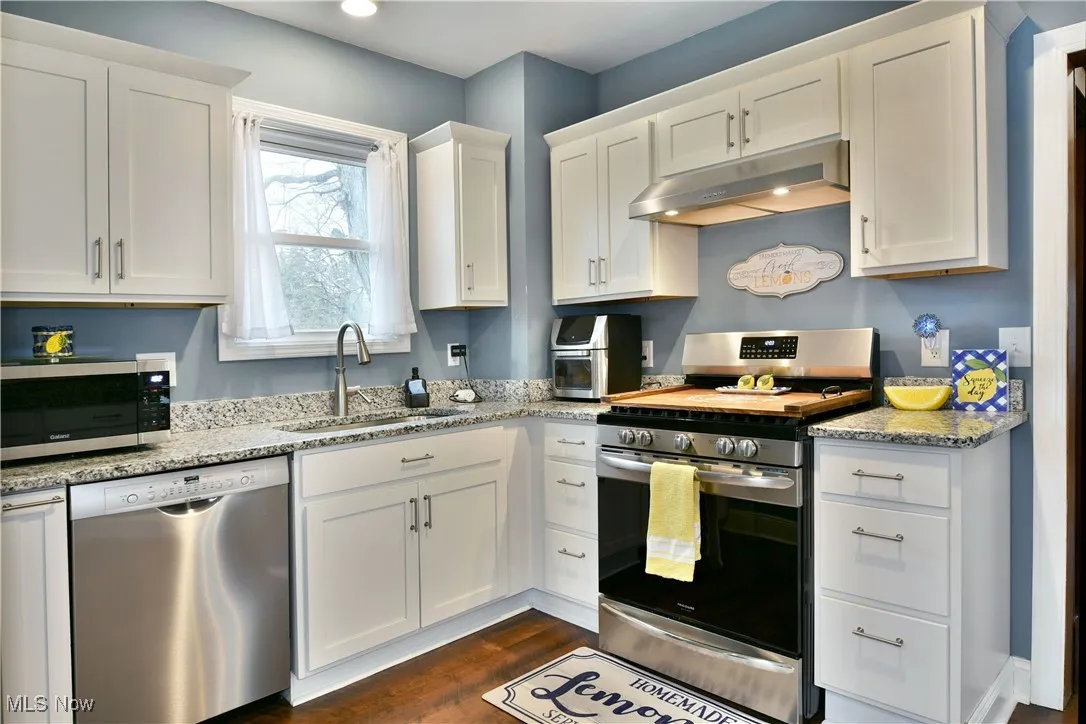 Kitchen with appliances with stainless steel finishes, white cabinetry, light stone countertops, under cabinet range hood, and recessed lighting