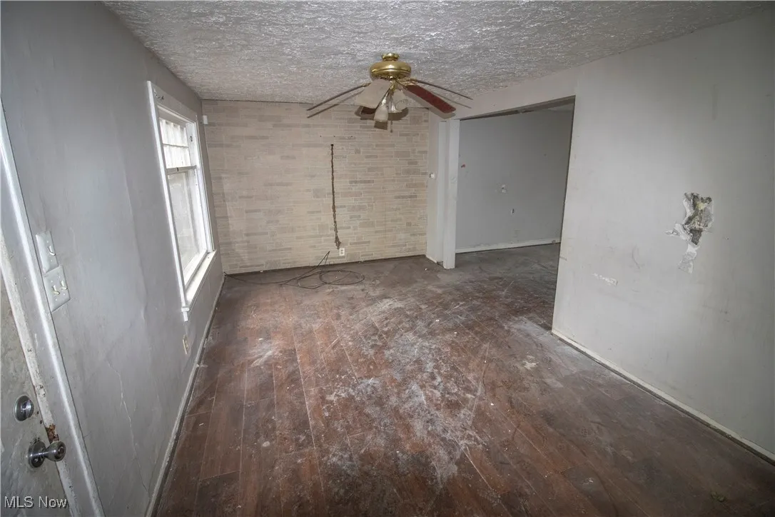 Unfurnished room featuring dark wood-type flooring, ceiling fan, a textured ceiling, and brick wall