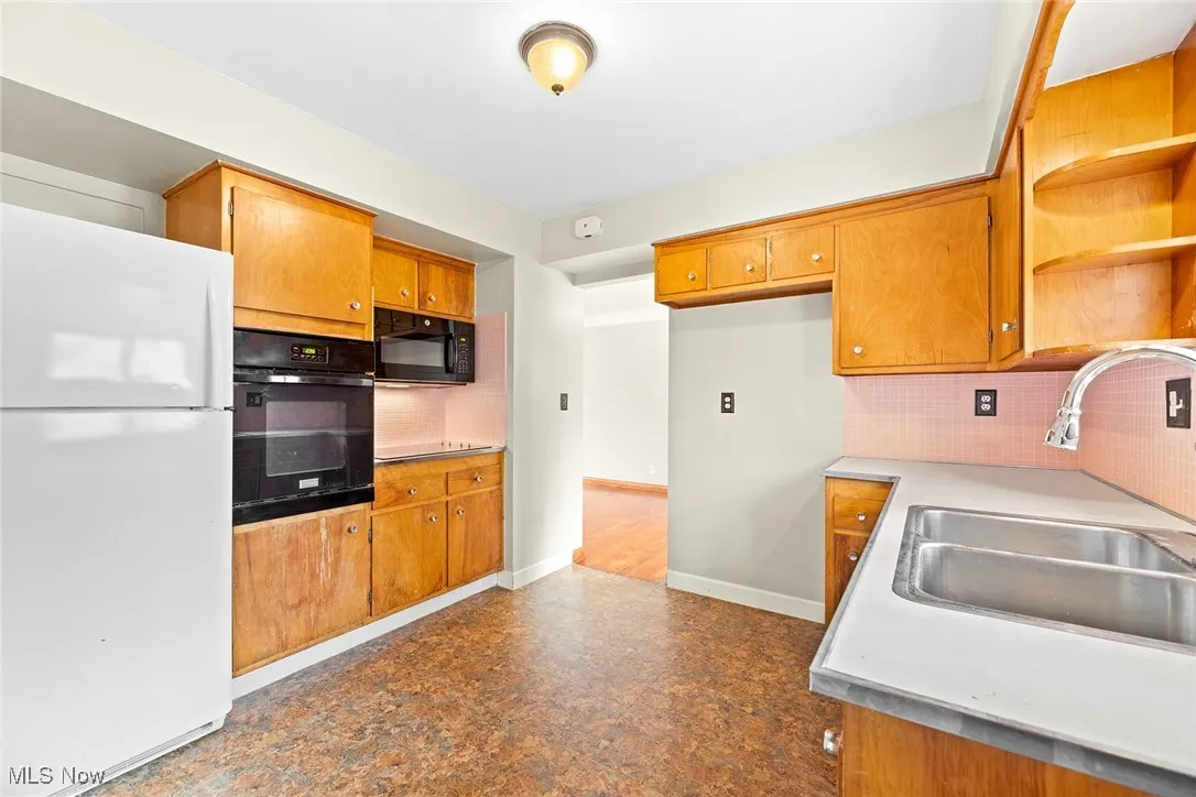 Kitchen with open shelves, black appliances, decorative backsplash, and light countertops