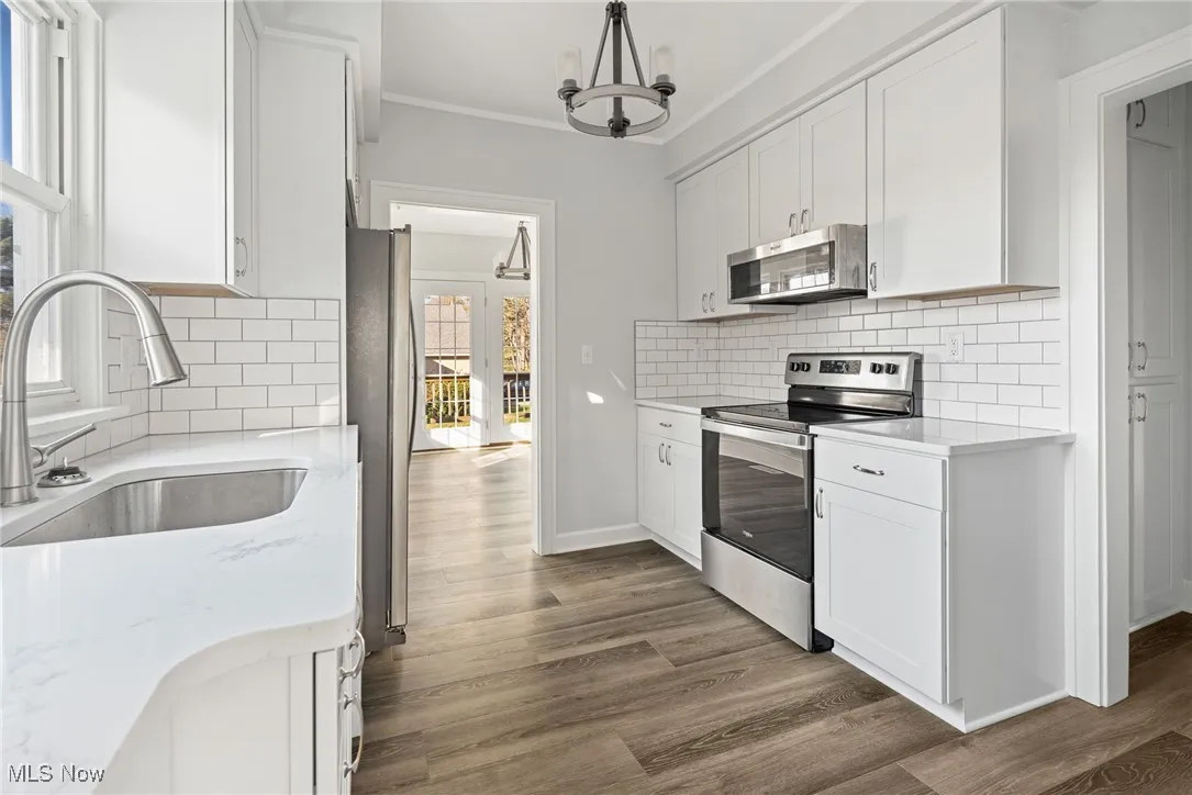 Kitchen featuring appliances with stainless steel finishes, decorative backsplash, a chandelier, white cabinets, and crown molding