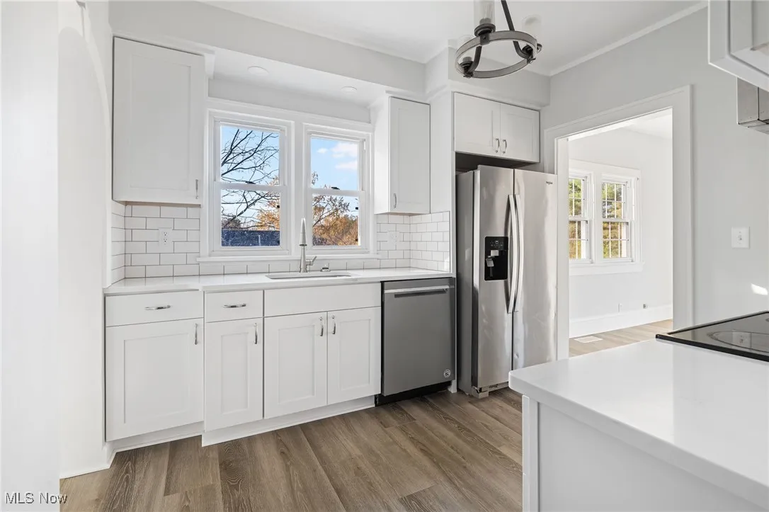 Kitchen with stainless steel appliances, white cabinetry, light wood-style floors, decorative backsplash, and crown molding