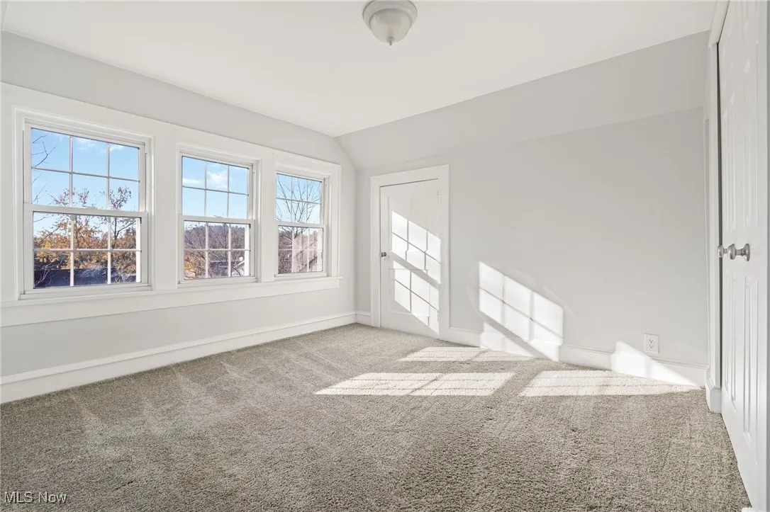 Unfurnished room with plenty of natural light, vaulted ceiling, and light carpet