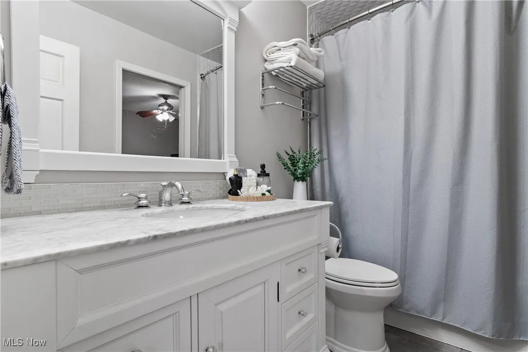 Full bath with vanity, a shower with curtain, ceiling fan, and backsplash