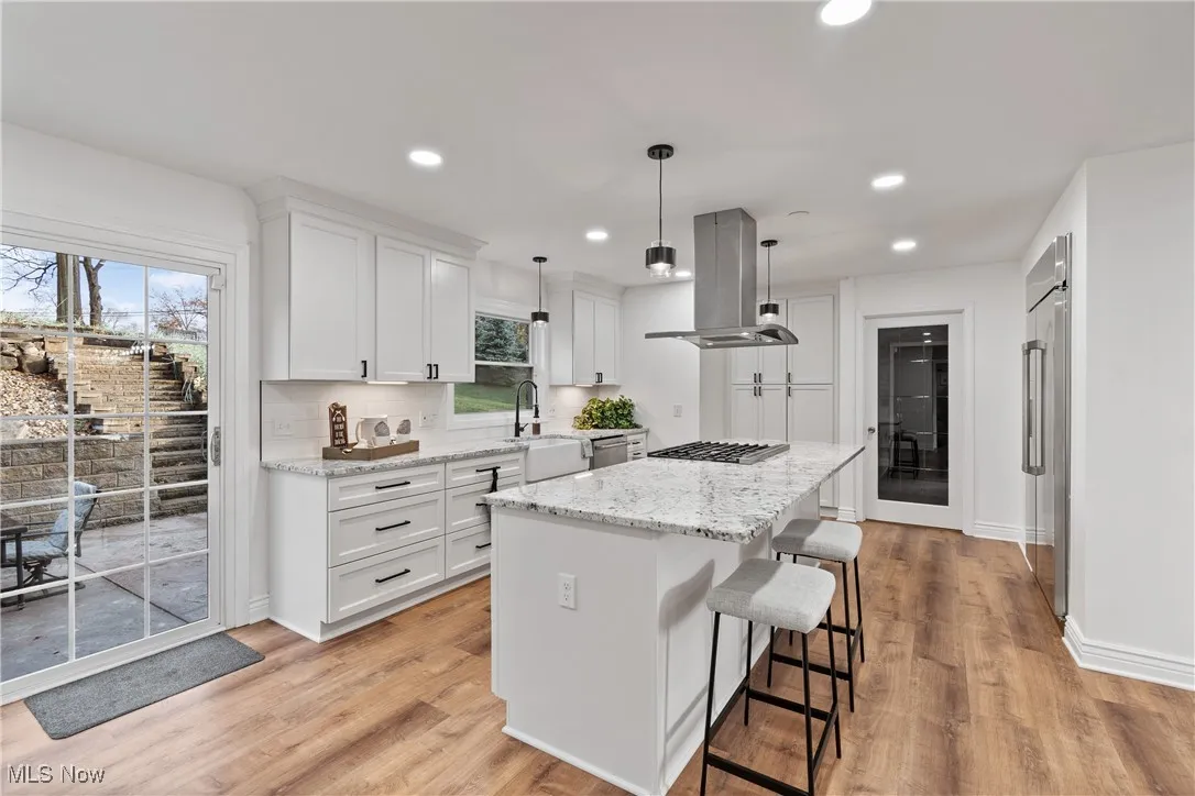 Kitchen with white cabinets, light stone counters, a kitchen breakfast bar, recessed lighting, and decorative light fixtures