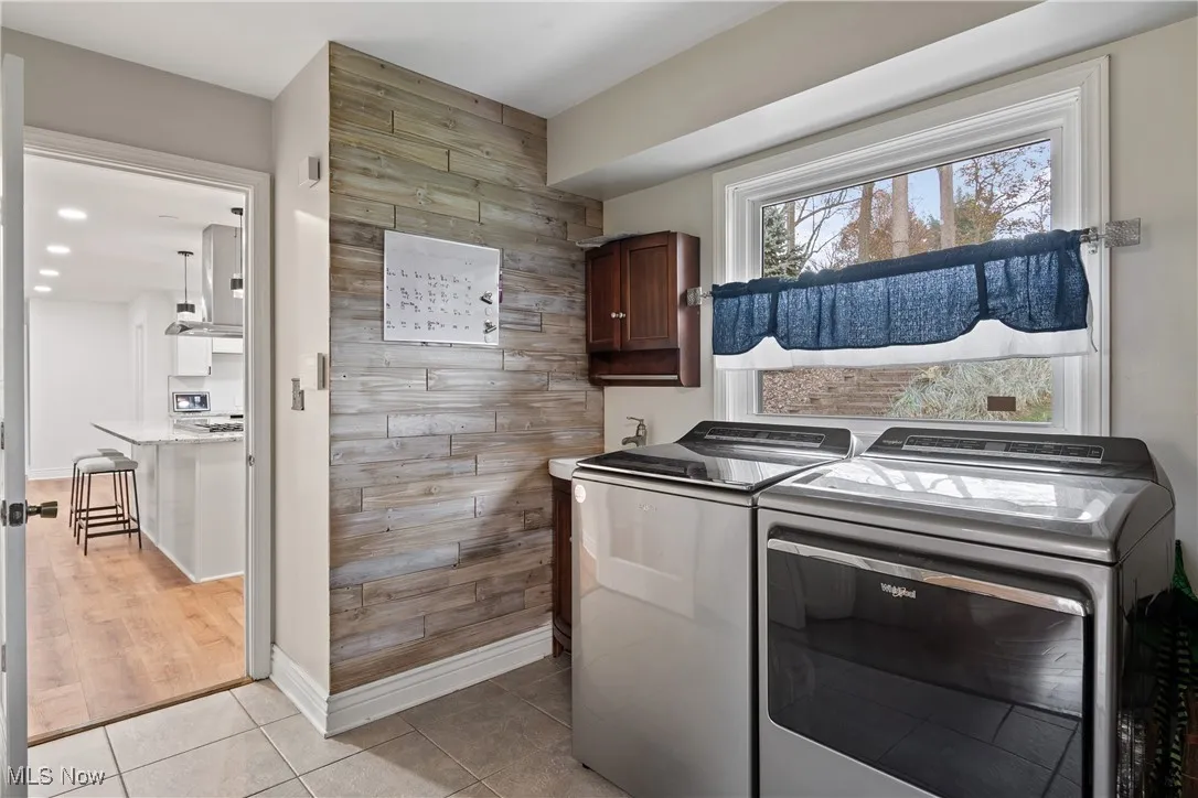 Laundry room with light tile patterned flooring, wood walls, washer and dryer, cabinet space, and recessed lighting