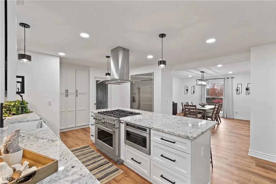 Kitchen with light stone counters, pendant lighting, white cabinetry, light wood-style floors, and recessed lighting