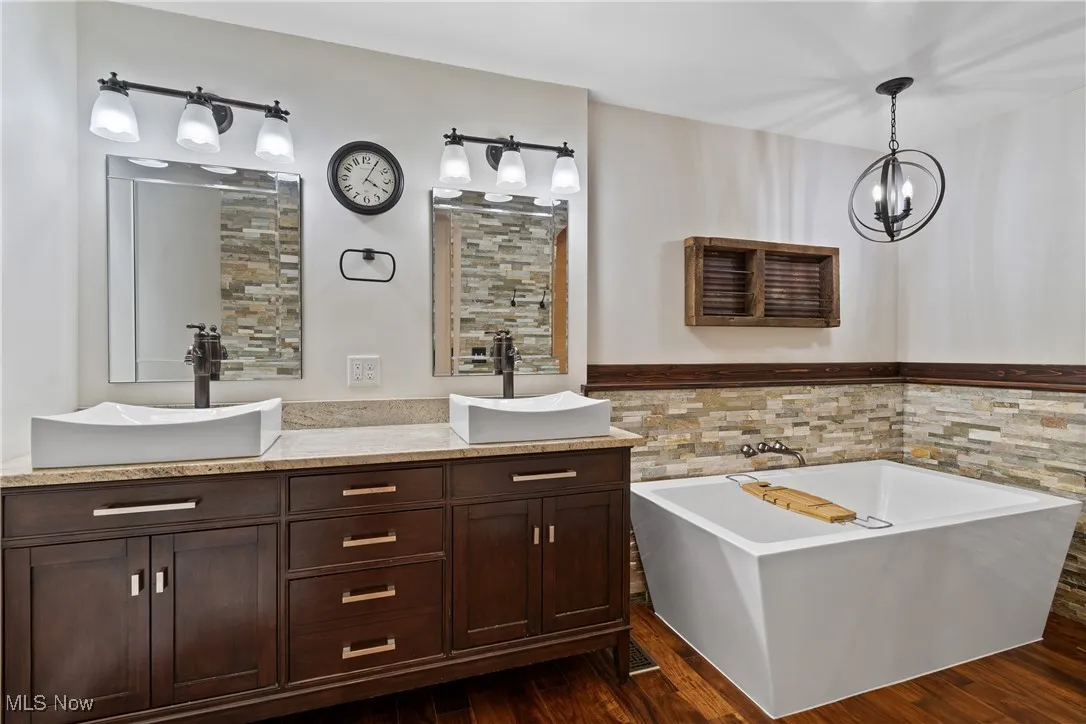 Bathroom with double vanity, a bath, dark wood-style flooring, tile walls, and a wainscoted wall