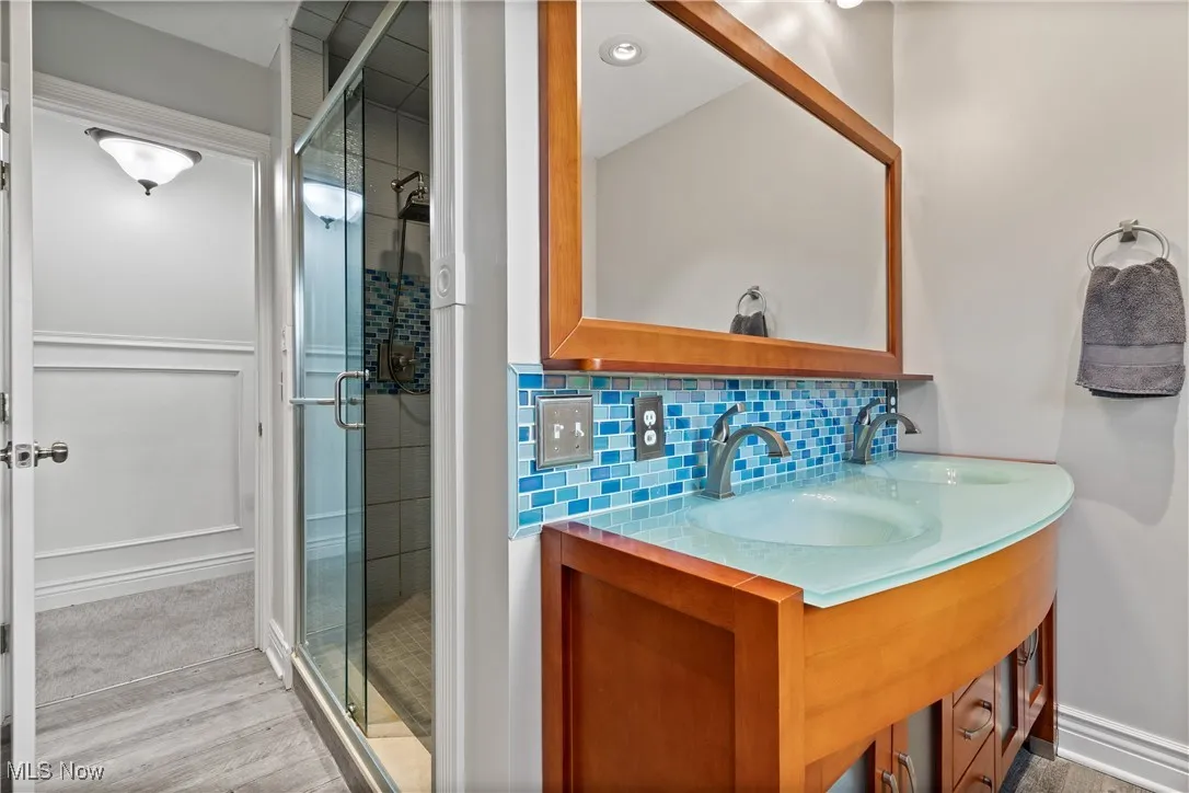 Full bathroom featuring tasteful backsplash, a shower stall, double vanity, and light wood-style flooring