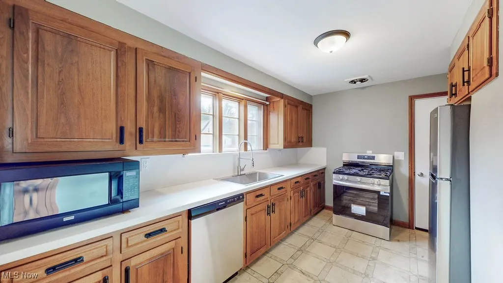 Kitchen with stainless steel appliances, brown cabinets, light countertops, and light flooring