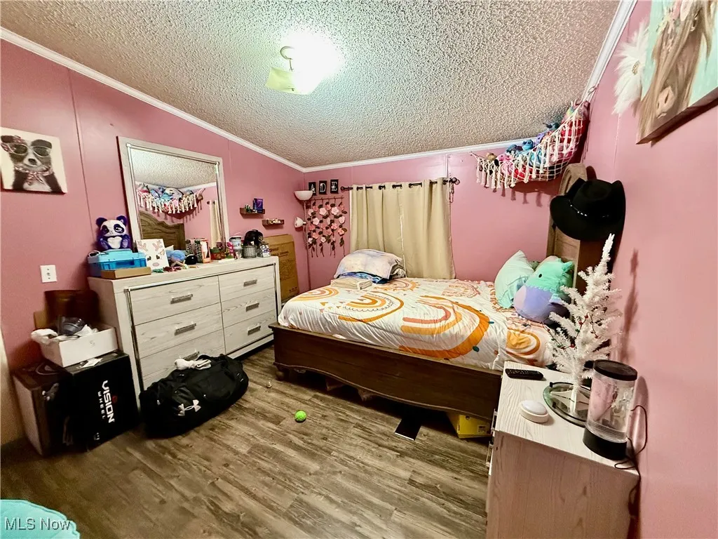 Bedroom featuring crown molding, lofted ceiling, a textured ceiling, and wood finished floors