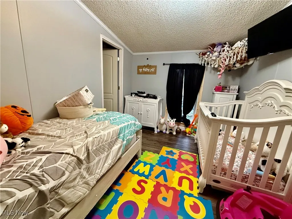Bedroom featuring a textured ceiling, dark wood-type flooring, and crown molding