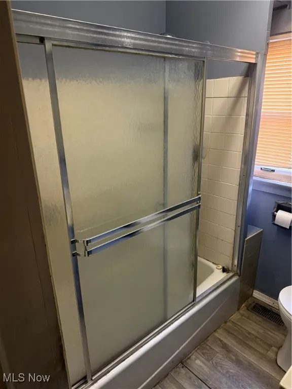 Bathroom featuring wood finished floors and enclosed tub / shower combo