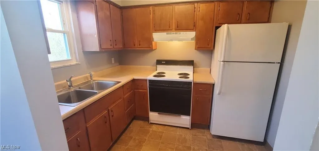 Kitchen with white appliances, light countertops, brown cabinets, and under cabinet range hood