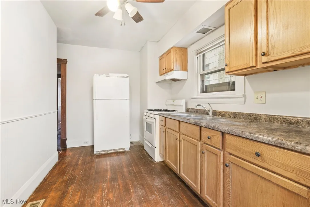 Kitchen with white appliances, dark wood finished floors, under cabinet range hood, ceiling fan, and light brown cabinets
