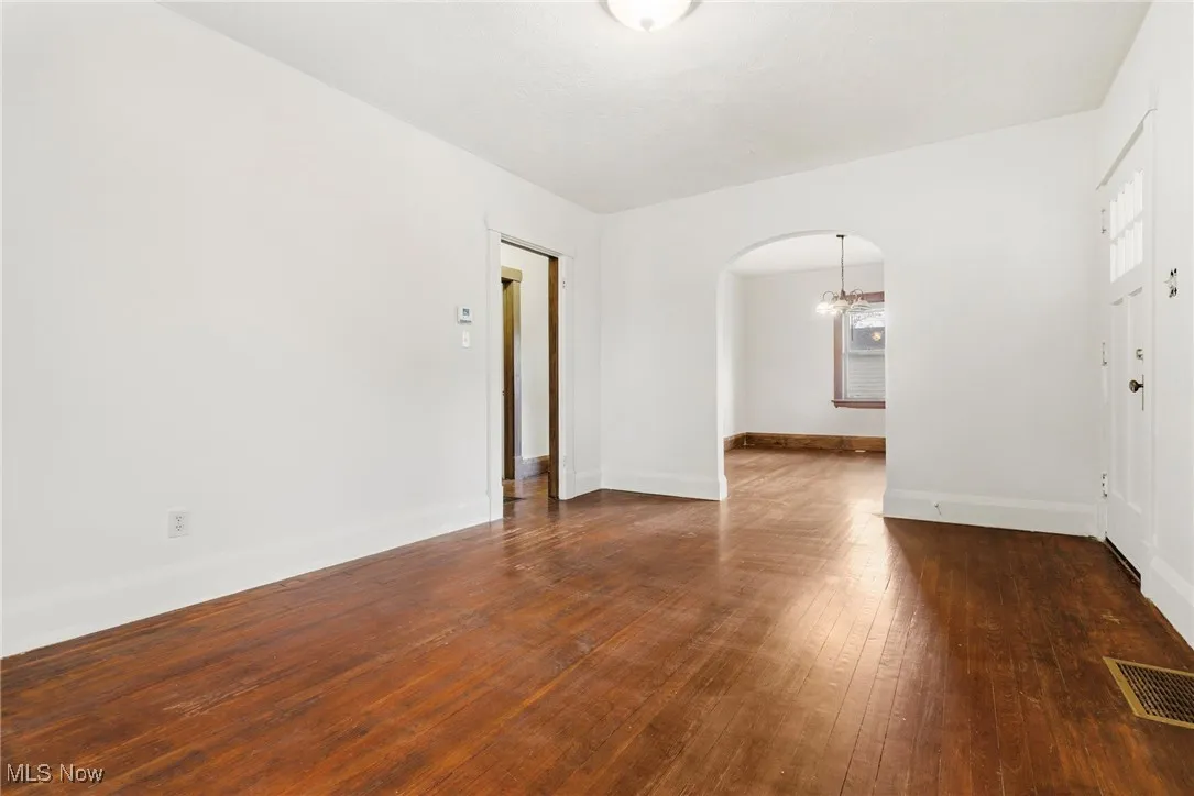Empty room featuring arched walkways, dark wood-style floors, and a chandelier