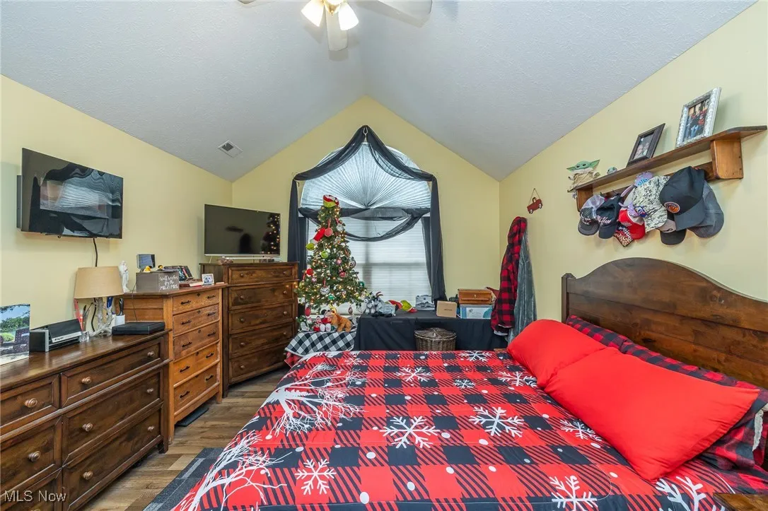 Bedroom featuring vaulted ceiling, wood finished floors, ceiling fan, and a textured ceiling