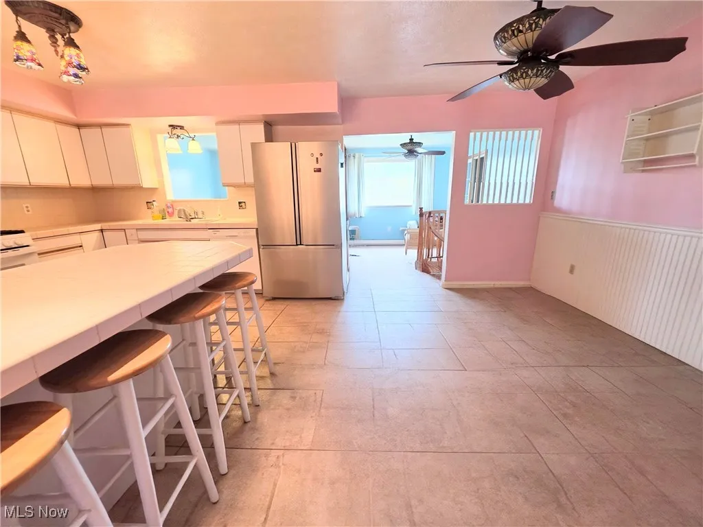 Kitchen featuring white cabinetry, white appliances, a kitchen breakfast bar, healthy amount of natural light, and a wainscoted wall