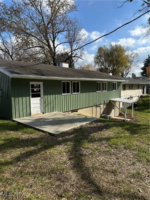 Rear view of property featuring a chimney, board and batten siding, a yard, a patio area, and a shingled roof