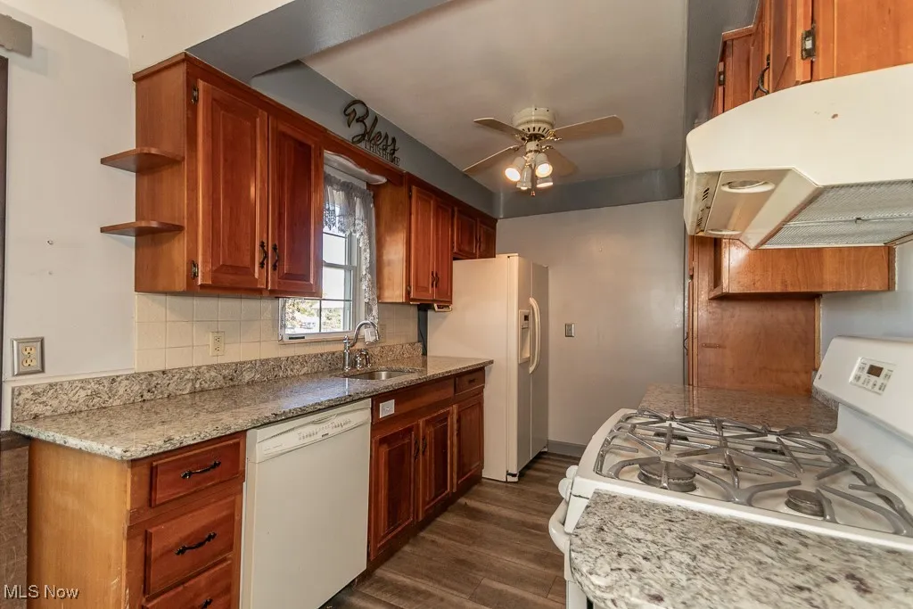 Kitchen featuring white appliances, open shelves, under cabinet range hood, dark wood-type flooring, and tasteful backsplash