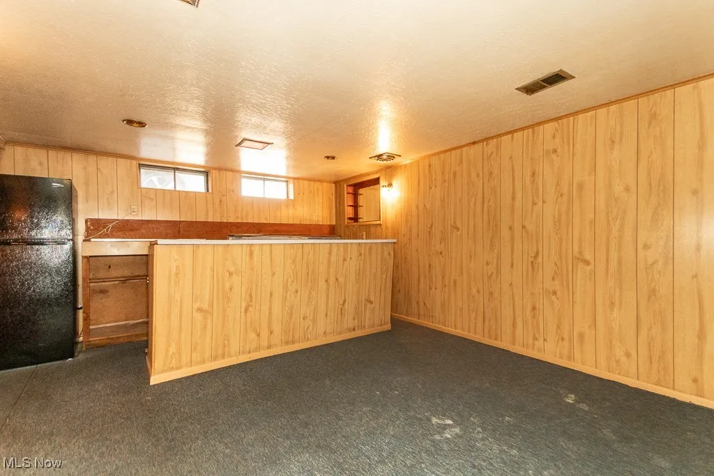 Kitchen with freestanding refrigerator, wood walls, light countertops, and a textured ceiling