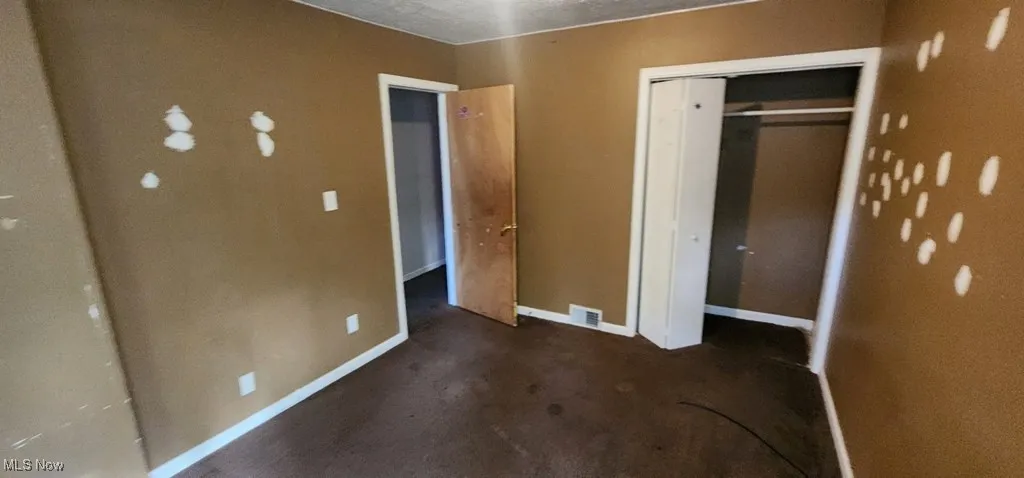 Unfurnished bedroom featuring a closet and dark carpet
