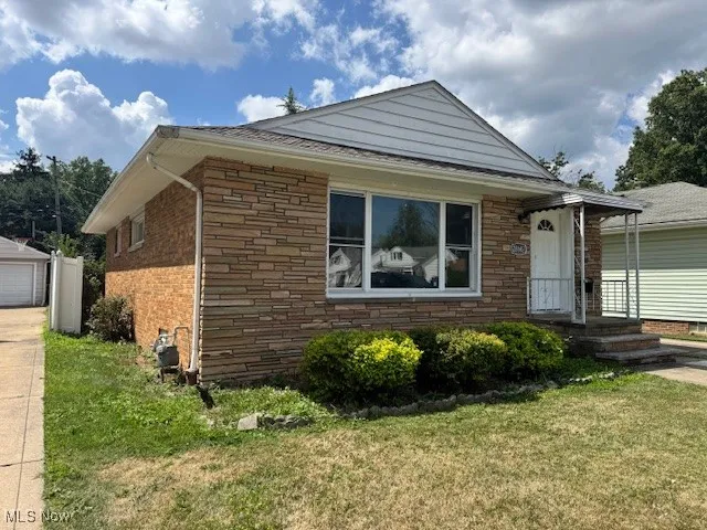 Ranch-style home featuring stone siding, a front lawn, and a two car detached garage