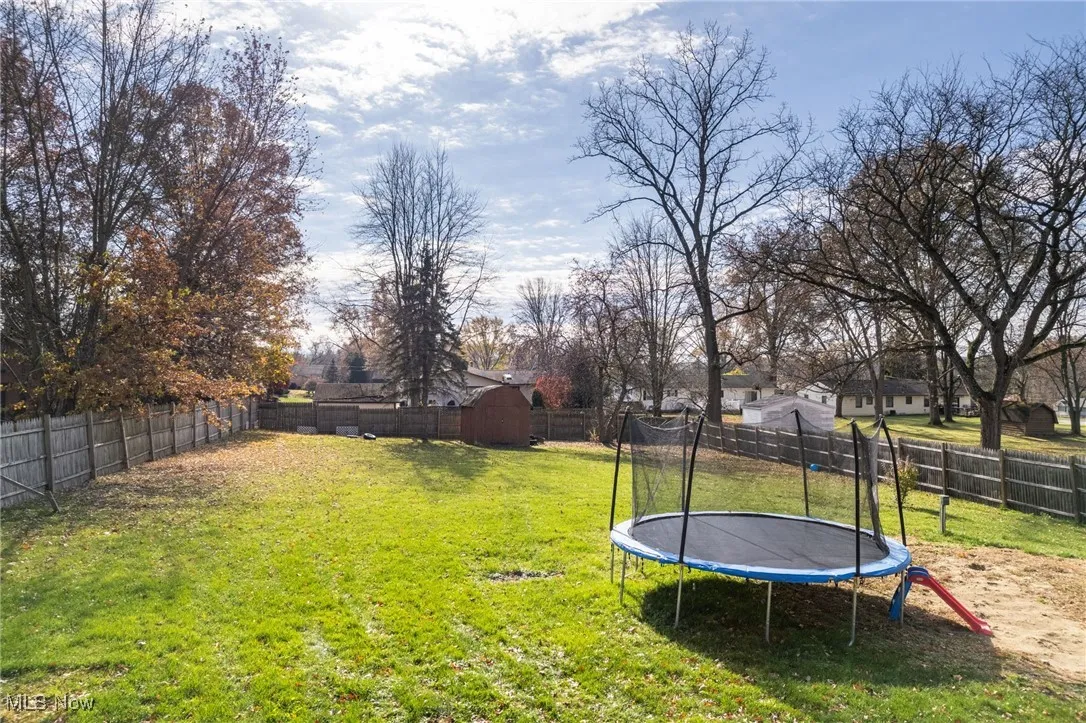 Fenced backyard featuring a trampoline and a storage shed