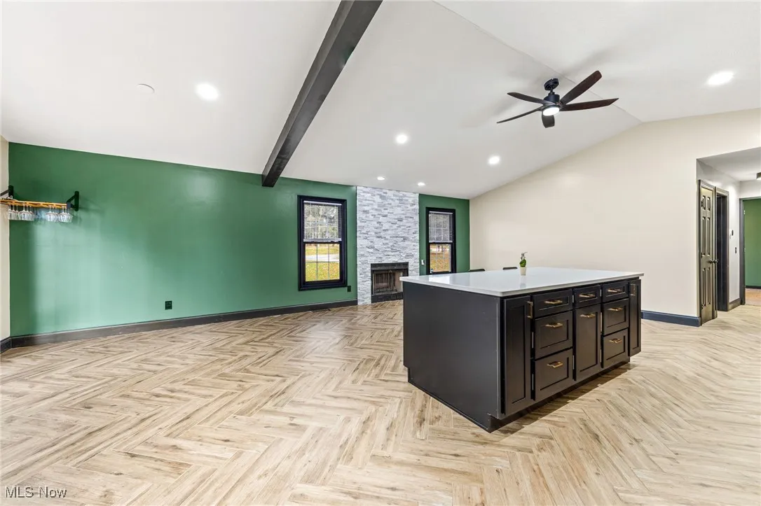 Kitchen with open floor plan, a center island with sink, dark cabinets, a large fireplace, and ceiling fan