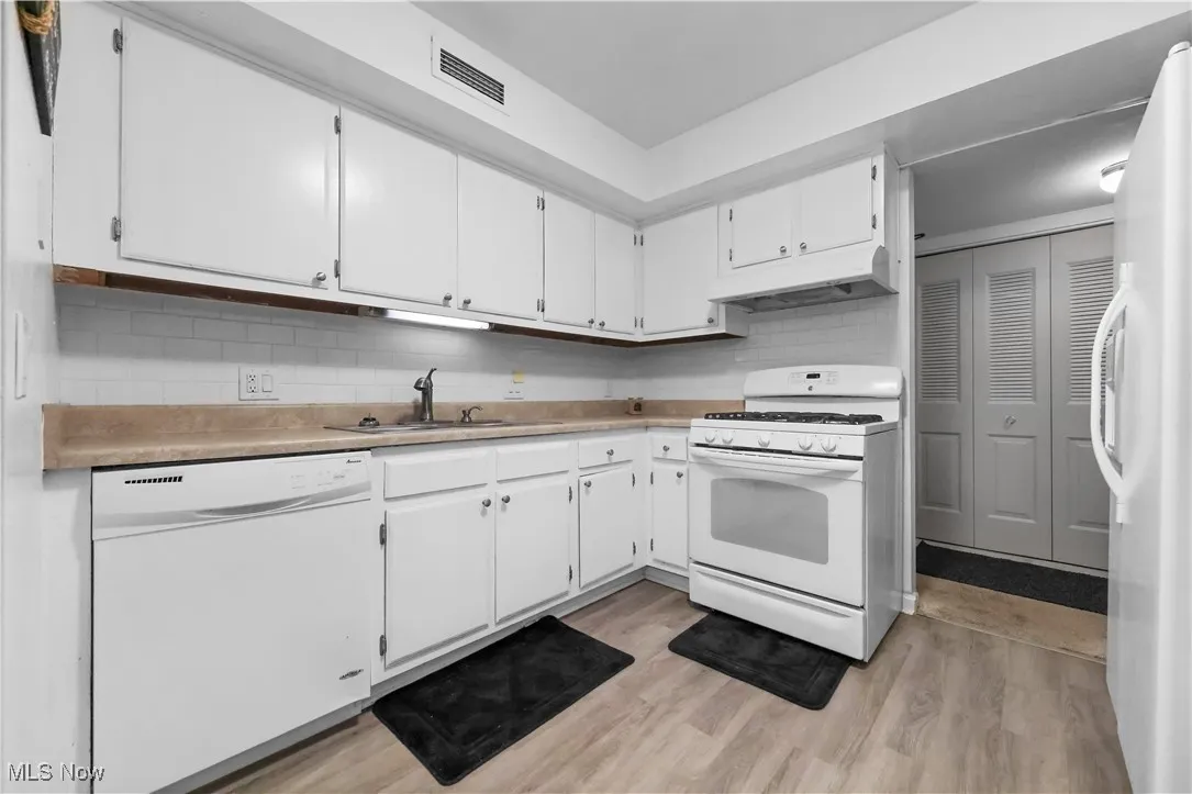Kitchen with white appliances, white cabinetry, tasteful backsplash, light countertops, and light wood finished floors