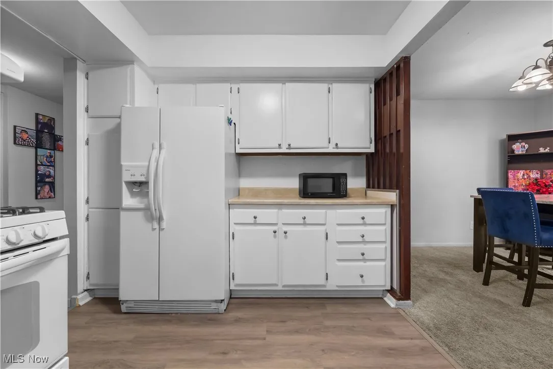 Kitchen featuring white cabinets, white appliances, light countertops, and light wood-type flooring