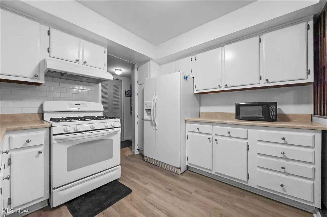 Kitchen with white appliances, light countertops, and white cabinetry