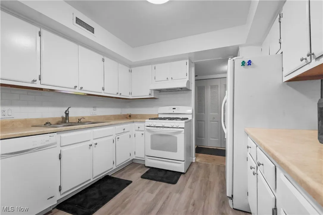 Kitchen featuring white appliances, light countertops, white cabinets, light wood-style flooring, and tasteful backsplash