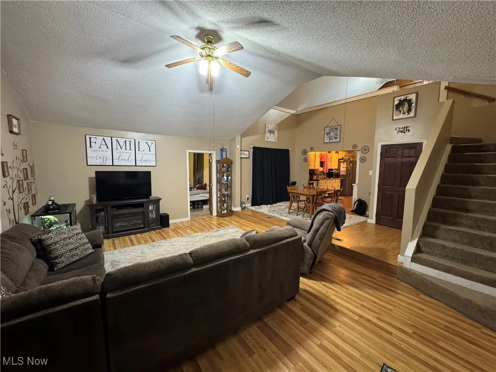 Living area with stairs, vaulted ceiling, wood finished floors, a ceiling fan, and a textured ceiling