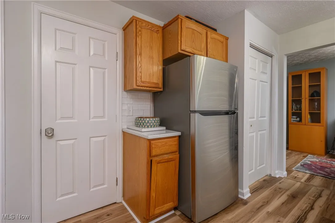 Kitchen featuring light countertops, freestanding refrigerator, a textured ceiling, light wood-style flooring, and backsplash