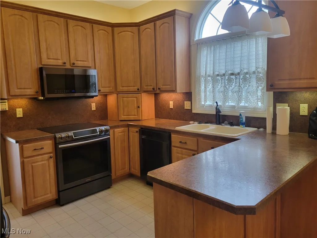 Kitchen featuring stainless steel appliances, a peninsula, tasteful backsplash, and brown cabinets