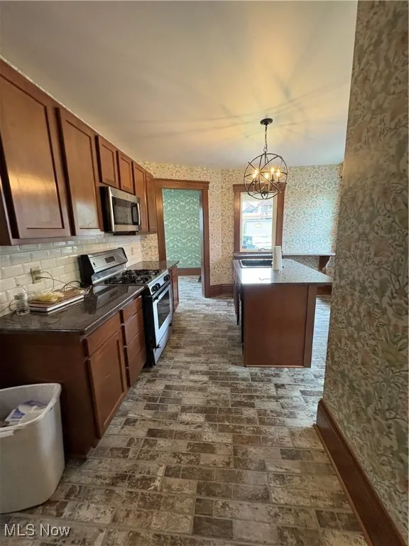 Kitchen featuring brick floor, range, a chandelier, wallpapered walls, and baseboards