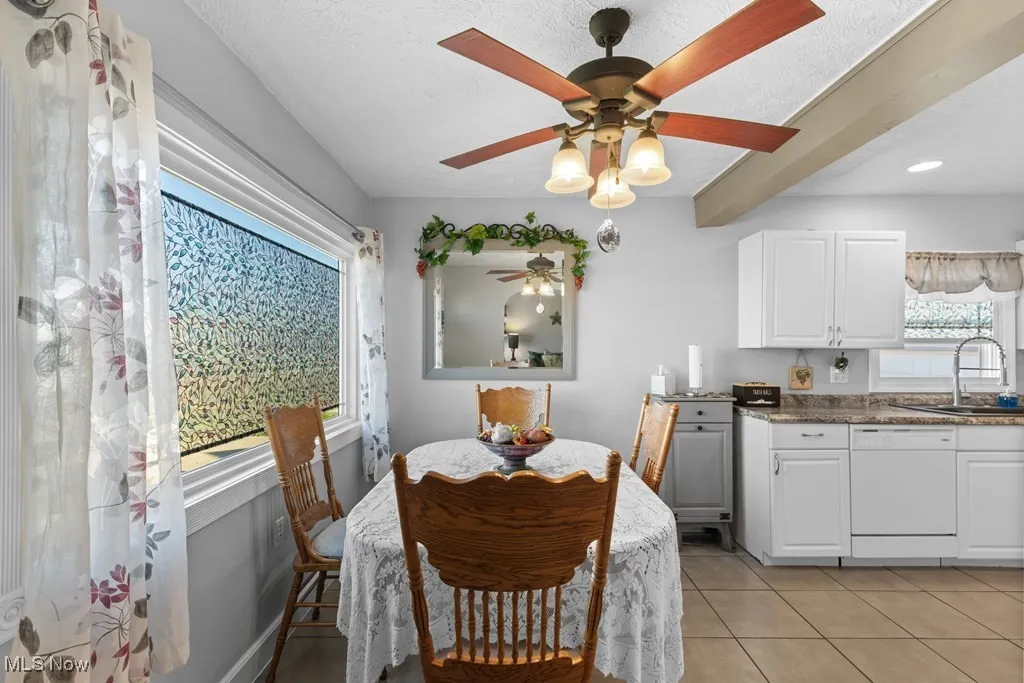 Dining space featuring light tile patterned flooring, a ceiling fan, beam ceiling, and a textured ceiling
