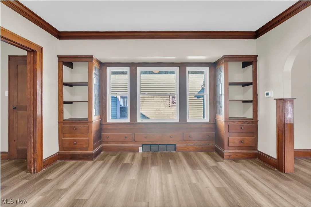 Empty room featuring crown molding, arched walkways, healthy amount of natural light, and light wood-style flooring