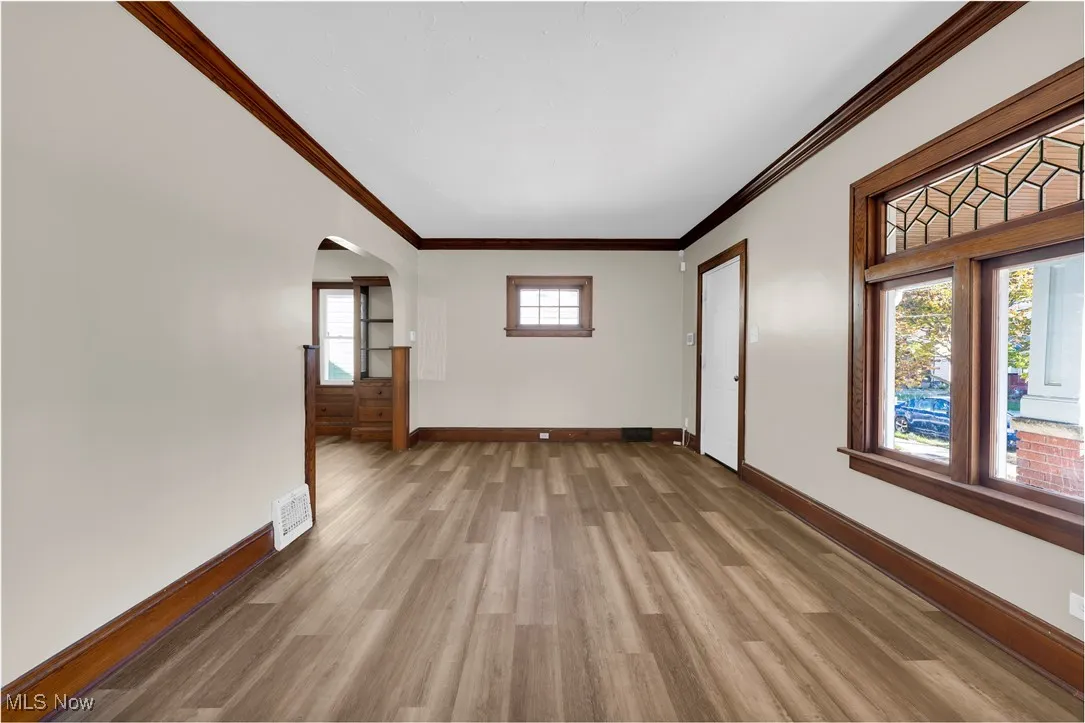 Empty room with arched walkways, crown molding, and wood finished floors